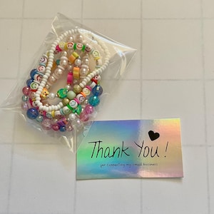 May include: A set of colorful beaded bracelets with smiley face charms. The bracelets are packaged in a clear plastic bag with a thank you card that reads "Thank You! for supporting my small business".