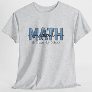 Op de afbeelding: Een lichtgrijs t-shirt met korte mouwen en het woord MATH in grote blauwe letters met een wit stippenpatroon. Het woord squad staat in zwarte cursieve letters in het midden, met daaronder de tekst Elk Grove High School.