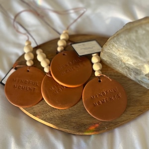 May include: Four brown leather car air fresheners with the text "Mindful Moments" on each. The fresheners are attached to wooden bead strings.