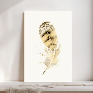 May include: Watercolor painting of a feather with a cream, tan, and brown color scheme. The feather has a detailed pattern at the top and a soft, wispy base. Small paint splatters add texture to the white background. The artwork is displayed on a white surface.