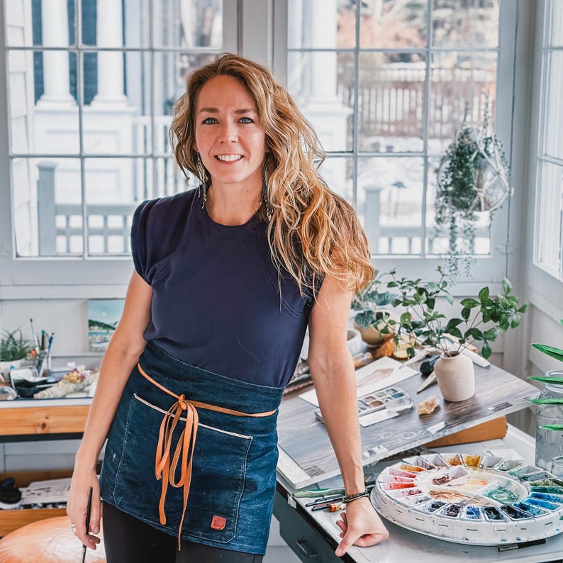 Shayna Larsen in her studio leaning with a blue apron.