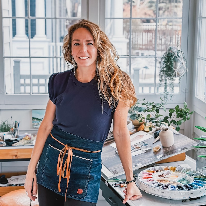 Shayna Larsen in her studio leaning with a blue apron.