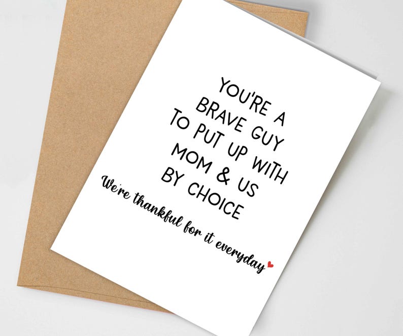May include: A white greeting card with black text that reads "YOU'RE A BRAVE GUY TO PUT UP WITH MOM & US BY CHOICE. We're thankful for it everyday" is placed on a brown envelope. A small red heart is at the end of the text.