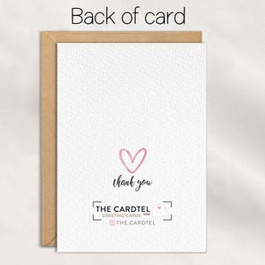 Op de afbeelding: De achterkant van een wenskaart met een getextureerd wit oppervlak. Een roze hart en de woorden "dank u" zijn gecentreerd. De onderkant toont het logo en de social media handle van "THE CARDTEL GREETING CARDS". De kaart zit in een bruine envelop.