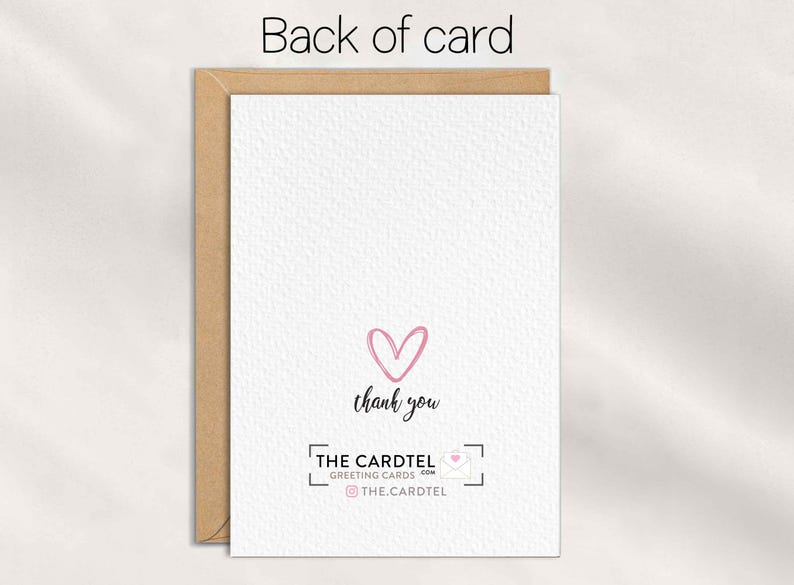 Op de afbeelding: De achterkant van een wenskaart met een getextureerd wit oppervlak. Een roze hart en de woorden "dank u" zijn gecentreerd. De onderkant toont het logo en de social media handle van "THE CARDTEL GREETING CARDS". De kaart zit in een bruine envelop.