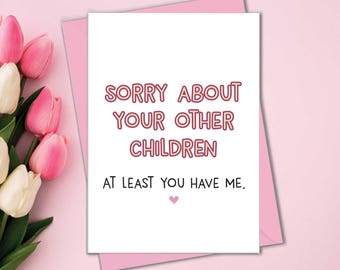 Puede incluir: Una tarjeta rosa y blanca con el texto "Lo siento por tus otros hijos. Al menos me tienes a mí." en letras rosas y rojas con contorno. Un pequeño corazón rosa se encuentra en la parte inferior de la tarjeta.