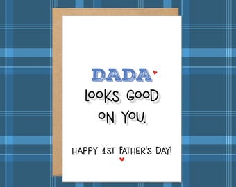 May include: A greeting card with a brown border and a white interior. The card reads "DADA looks GOOD ON YOU." in black text, with the word "DADA" in blue. The card also says "HAPPY 1ST FATHER'S DAY!" with a small red heart.
