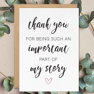 Puede incluir: Una tarjeta de agradecimiento con fondo blanco y borde marrón. La tarjeta presenta texto negro en cursiva que dice "gracias por ser una parte tan importante de mi historia" con un pequeño corazón rosa en la parte inferior. Hojas de eucalipto rodean la tarjeta.