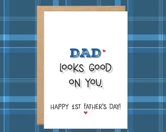 May include: A Father's Day greeting card with a white background and a brown border. The card reads "DAD looks GOOD ON YOU." and "HAPPY 1ST FATHER'S DAY!" in black text. The word "DAD" is in blue with a red heart.