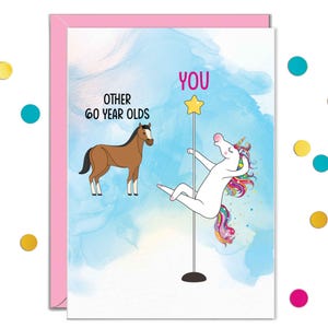 May include: A greeting card with a pink border features a humorous illustration. It shows a brown horse labeled "Other 60 Year Olds" and a unicorn pole dancing labeled "YOU". The background is a watercolor wash of blue and white.