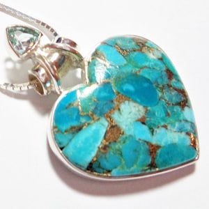 May include: A silver heart-shaped pendant with a turquoise and gold inlay. The pendant is attached to a silver chain.