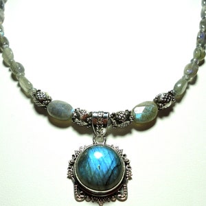 May include: A silver necklace with a large, round, iridescent blue labradorite gemstone pendant. The necklace is made with silver beads and oval-shaped labradorite stones.
