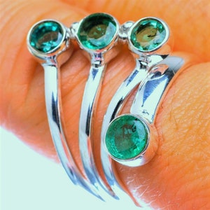 May include: A silver ring with four green gemstones. The ring is designed with three bands that wrap around the finger.