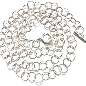 May include: A silver-colored necklace composed of interconnected textured circles. The necklace features a toggle clasp closure. The design is simple and elegant, suitable for everyday wear or special occasions.
