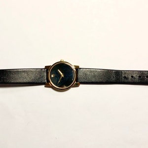 May include: A gold-tone wristwatch with a black face and black leather band.