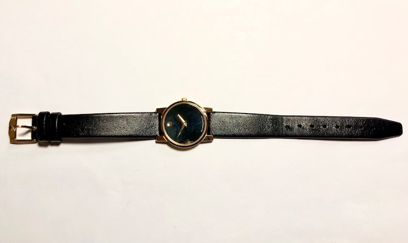 May include: A gold-tone wristwatch with a black face and black leather band.