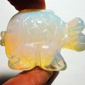 May include: A translucent iridescent opal fish figurine with a detailed, textured surface. The fish has a rounded body and a tail fin.