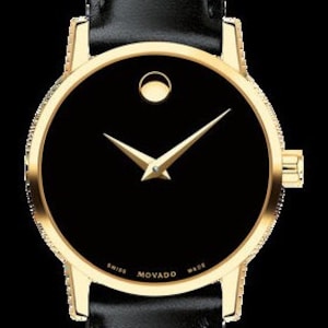 May include: A gold-tone wristwatch with a black face and a single gold hand. The watch face has a small circle at the 12 o'clock position and the words "SWISS MOVADO MADE" printed around the edge.