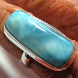 May include: A rectangular, polished light blue stone set in a smooth silver band. The stone features cloudy white and cyan marbling throughout its surface. The ring is designed with a simple, clean metal setting that frames the elongated gemstone.