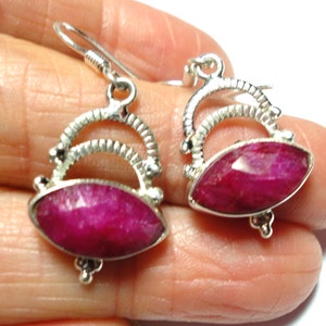 May include: A pair of silver earrings with pink gemstone drops. The earrings have a delicate, ornate design with a curved silver bar and a small, round accent at the bottom.