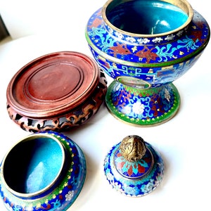 May include: A blue and green cloisonn&eacute; incense burner with a lid and a wooden stand. The burner has a floral design and is decorated with gold accents.