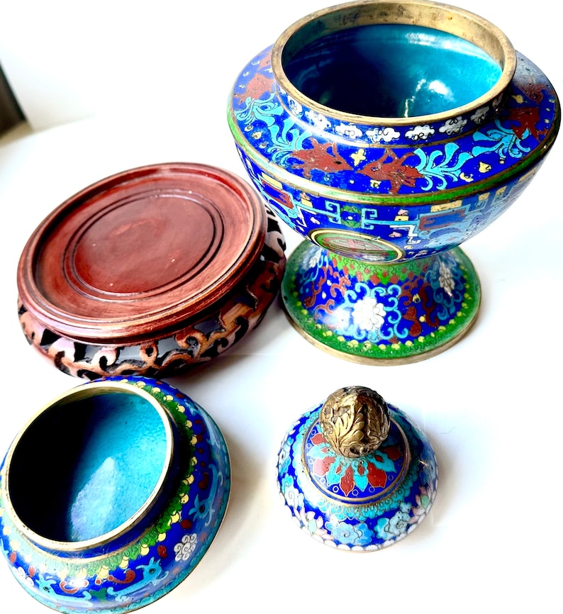 May include: A blue and green cloisonn&eacute; incense burner with a lid and a wooden stand. The burner has a floral design and is decorated with gold accents.