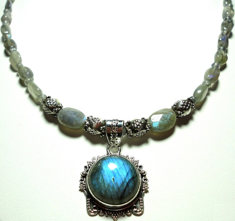 May include: A silver necklace with a large, round, iridescent blue labradorite gemstone pendant. The necklace is made with silver beads and oval-shaped labradorite stones.