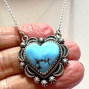 May include: A silver necklace featuring a heart-shaped turquoise pendant. The turquoise stone has brown veining and is set in a decorative silver frame with a chain. The pendant is surrounded by silver accents.