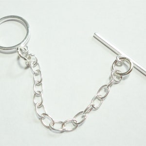 May include: Silver chain with a toggle clasp and a jump ring. The chain is made of oval links.