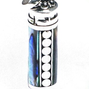 May include: A silver-toned cylindrical pendant with a decorative top. The pendant's body features a vertical row of white circles and iridescent abalone shell accents. The top has a detailed design.