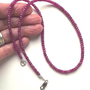 May include: A necklace composed of small, faceted, deep pinkish-red gemstone beads strung in a continuous line. The strand features a silver-toned metal toggle clasp at one end and a lobster claw clasp at the other, providing a secure closure.