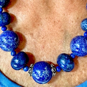 May include: A necklace made of large, round, blue lapis lazuli beads with silver accents. The beads are polished and have a marbled appearance.