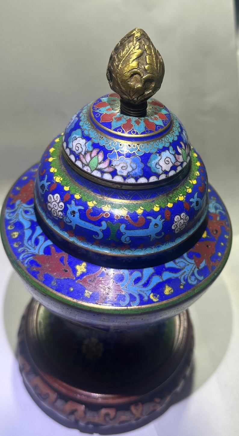May include: A blue and gold cloisonn&eacute; incense burner with a floral and cloud design. The burner has a wooden base and a gold finial.