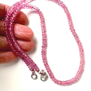 May include: A delicate pink gemstone necklace. The necklace is composed of small, round, pink beads strung together. The necklace has a silver clasp. The beads are a vibrant pink color, and the necklace is displayed against a white background.