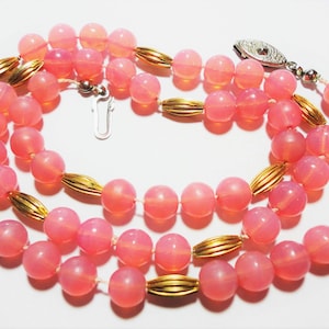 May include: A pink glass bead necklace with gold accents. The necklace is made of round beads and has a silver clasp.