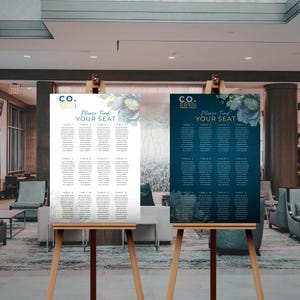 May include: Two wedding seating charts on easels. The chart on the left has a white background with blue floral accents. The chart on the right has a dark blue background with gold floral accents. Both charts have the text "Please Find Your Seat" and list tables and guest names.