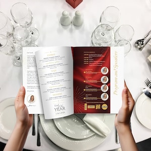 Può includere: Una persona tiene in mano un programma dell'evento aperto con un design rosso e oro. Il programma elenca il programma dell'evento, gli oratori e il menu, inclusi piatti come Smoked Salmon Rosette e Lasagna di verdure arrosto. L'evento è il "Gala di fine anno 202X".