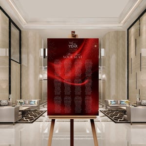 Puede incluir: Un plano de asientos rojo y dorado sobre un caballete. El gráfico dice "Fin de Año Gala 2023" y "Por favor, encuentra tu asiento". Los nombres están listados bajo los números de mesa. El fondo tiene un diseño de tela roja con fuegos artificiales dorados.