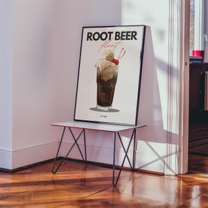 May include: A white poster with black text that reads "ROOT BEER float" and a drawing of a root beer float with a cherry on top. The poster is on a black metal table with a white top.