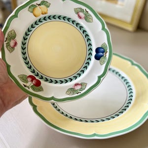 May include: Two white ceramic plates with scalloped edges. The plates have a yellow center, a green border, and a decorative ring of green leaves. Each plate is adorned with illustrations of fruits, including cherries, plums, and pears.