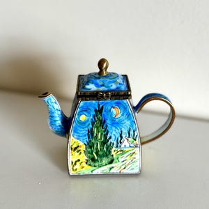 May include: A miniature teapot featuring a painting of a starry night scene with a tall cypress tree, a crescent moon, and a small house. The teapot has a blue and gold color scheme with a hinged lid and a curved handle.