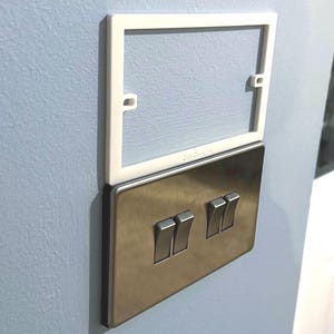 Puede incluir: Una placa de pared de plástico blanco con un interruptor de luz de níquel cepillado con tres interruptores de palanca.
