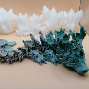 May include: An assortment of decorative objects, including white crystal formations and several succulent-like sculptures in shades of green and blue. The objects are arranged on a neutral-toned surface.