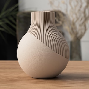 May include: A beige ceramic vase with a textured, spherical body and a ridged neck. The ridges are vertical and create a striped pattern. The vase is on a wooden surface.