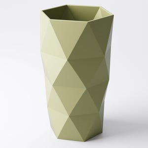 Op de afbeelding: Een saliegroene, geometrische vaas met een facetontwerp. De vaas heeft een zeshoekige bovenkant en een reeks ruitvormige facetten die een textuur cre&euml;ren. De vaas is effen van kleur en staat rechtop tegen een witte achtergrond.