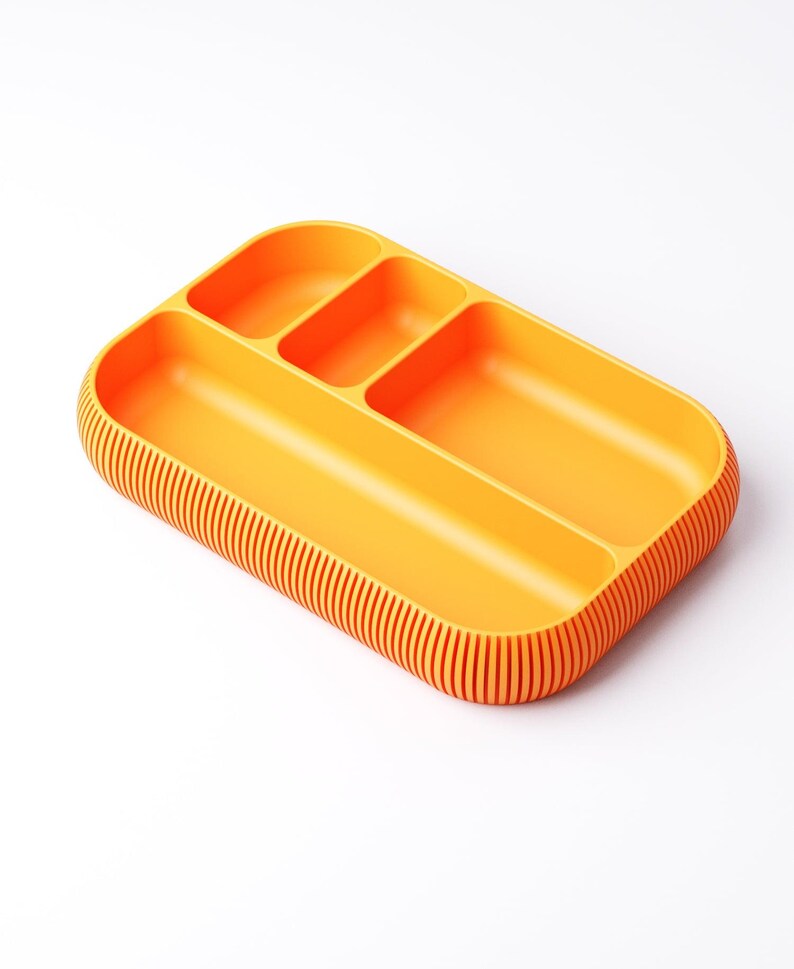 May include: An orange rectangular tray with three compartments and a ribbed edge. The tray is made of a solid, opaque material and is designed for organizing items. The compartments are different sizes.