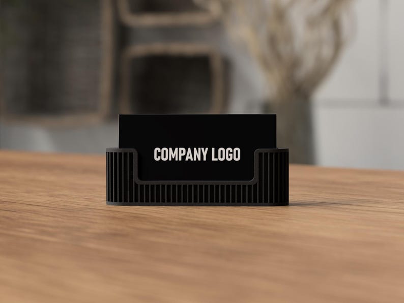 May include: A black business card holder with a vertical ribbed design. The holder displays a black business card with the text "COMPANY LOGO" in white. The holder sits on a wooden surface.