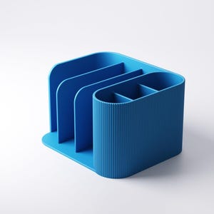 May include: A blue desk organizer with multiple compartments. The organizer has a curved design with vertical ridges on one side and dividers for organization. The base is flat, and the color is a solid, vibrant blue.
