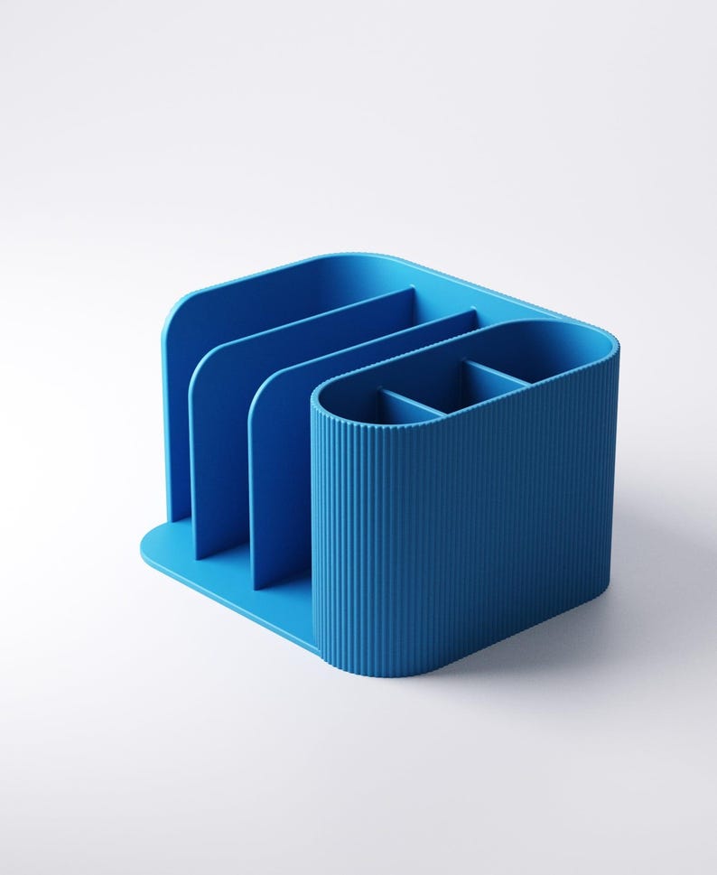 May include: A blue desk organizer with multiple compartments. The organizer has a curved design with vertical ridges on one side and dividers for organization. The base is flat, and the color is a solid, vibrant blue.