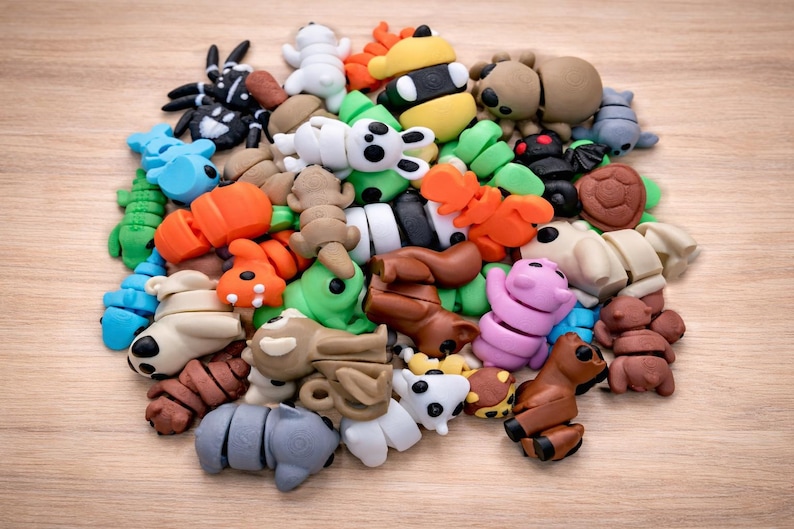 May include: A collection of colorful animal-shaped erasers in various colors, including brown, white, blue, orange, green, and pink. The erasers are arranged in a pile on a light brown wooden surface.